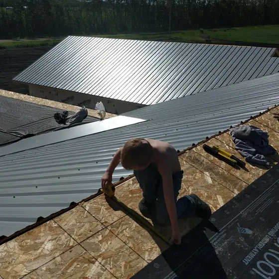 Measuring metal panels over fresh underlayment on a farm-building re-roof